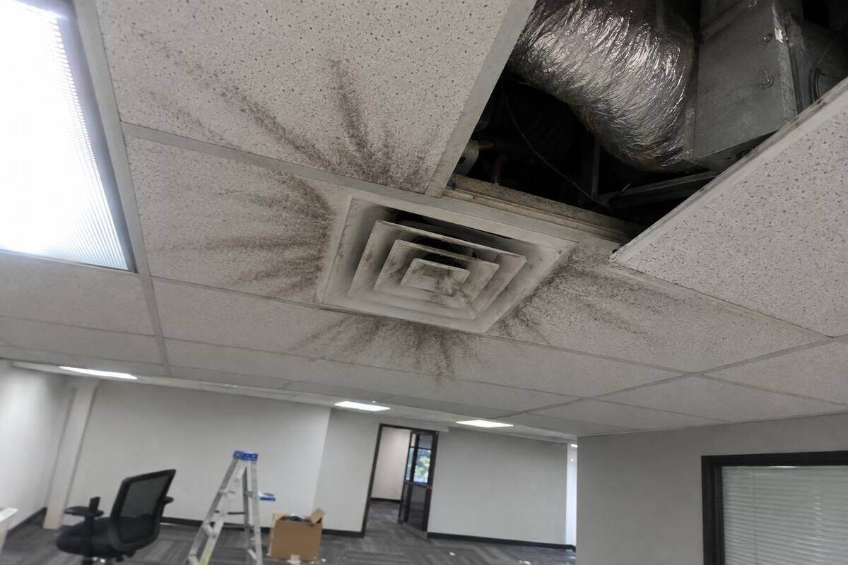A square ceiling diffuser in an office drop ceiling with dark dust streaks fanning across the tiles around it