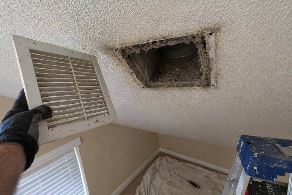 A ceiling supply register held aside with a ring of gray dust around the open duct boot above it